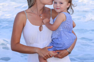mom kissing daughter on the beach