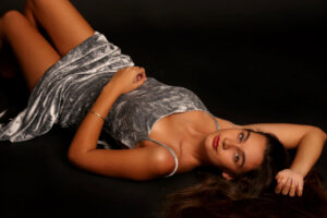 Beautiful girl in silver dress lying on her back facing the camera in photographic studio